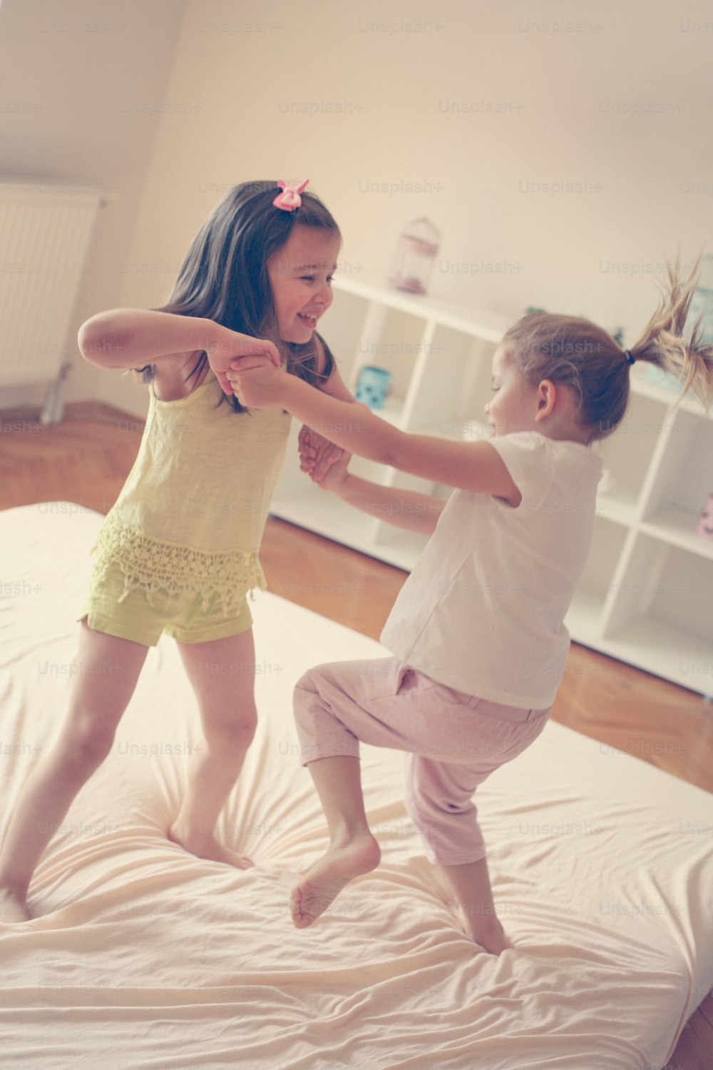 Little girls playing together in bed. Two little girls jumping on bed.