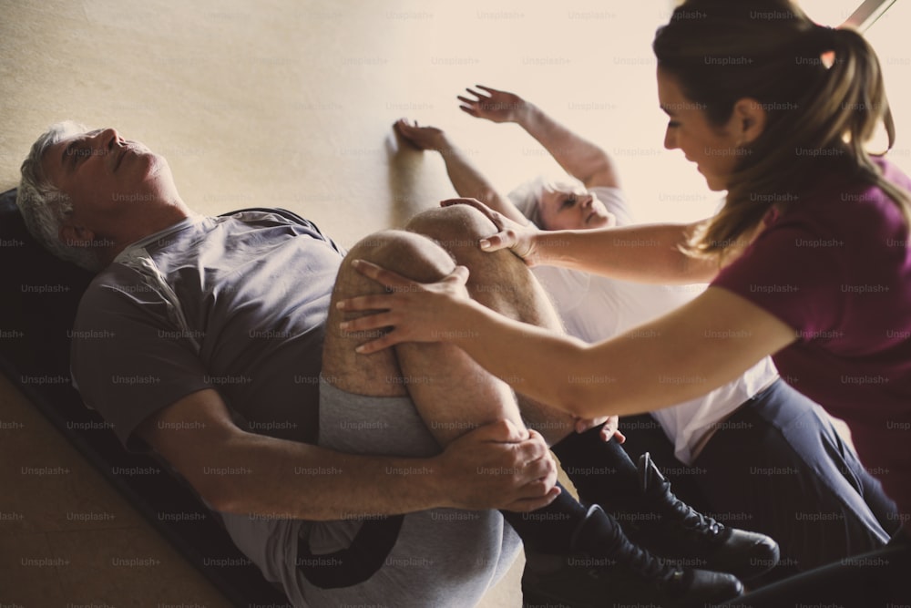 Allenamento di coppia senior in un centro di riabilitazione. Il personal trainer aiuta una coppia di anziani a fare stretching sul pavimento.
