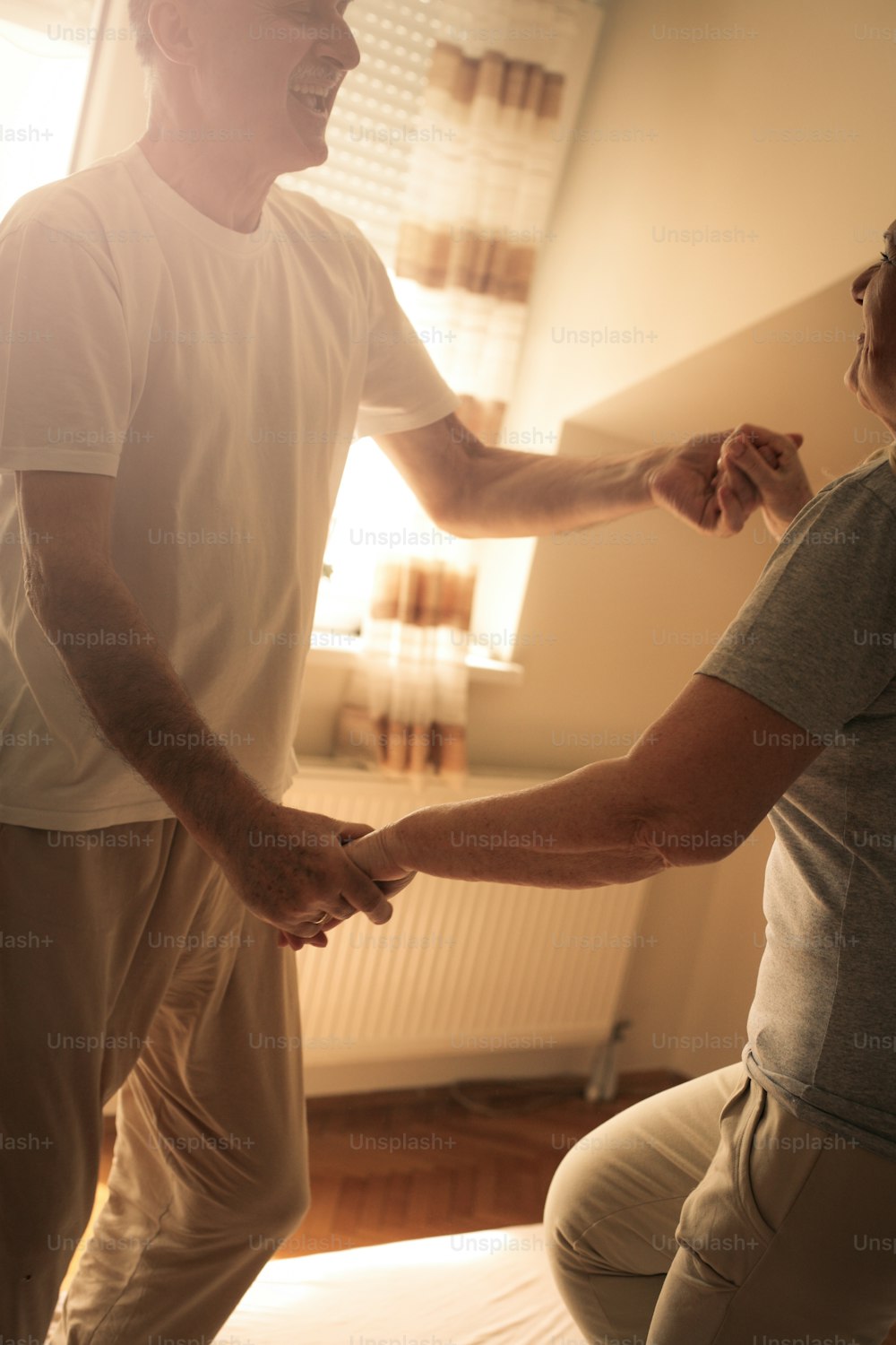 Coppia anziana che balla e salta insieme sul letto tenendosi per mano.