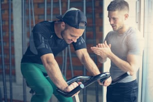 Un joven hace ejercicio en bicicletas estáticas en la clase de gimnasia. Entrenamiento de hombre en el gimnasio. Ejercicio en máquina elíptica. Entrenador personal de hombre.