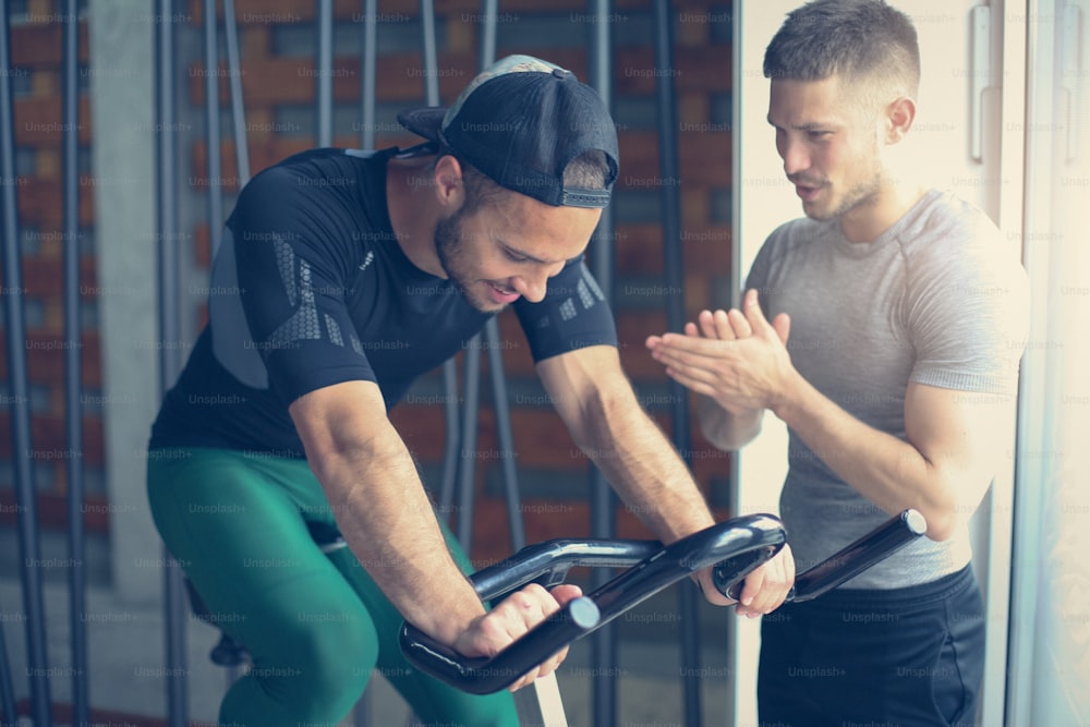 Young man exercise on stationary bikes in fitness class. Man workout in gym. Exercise on elliptical machine. Man personal trainer.