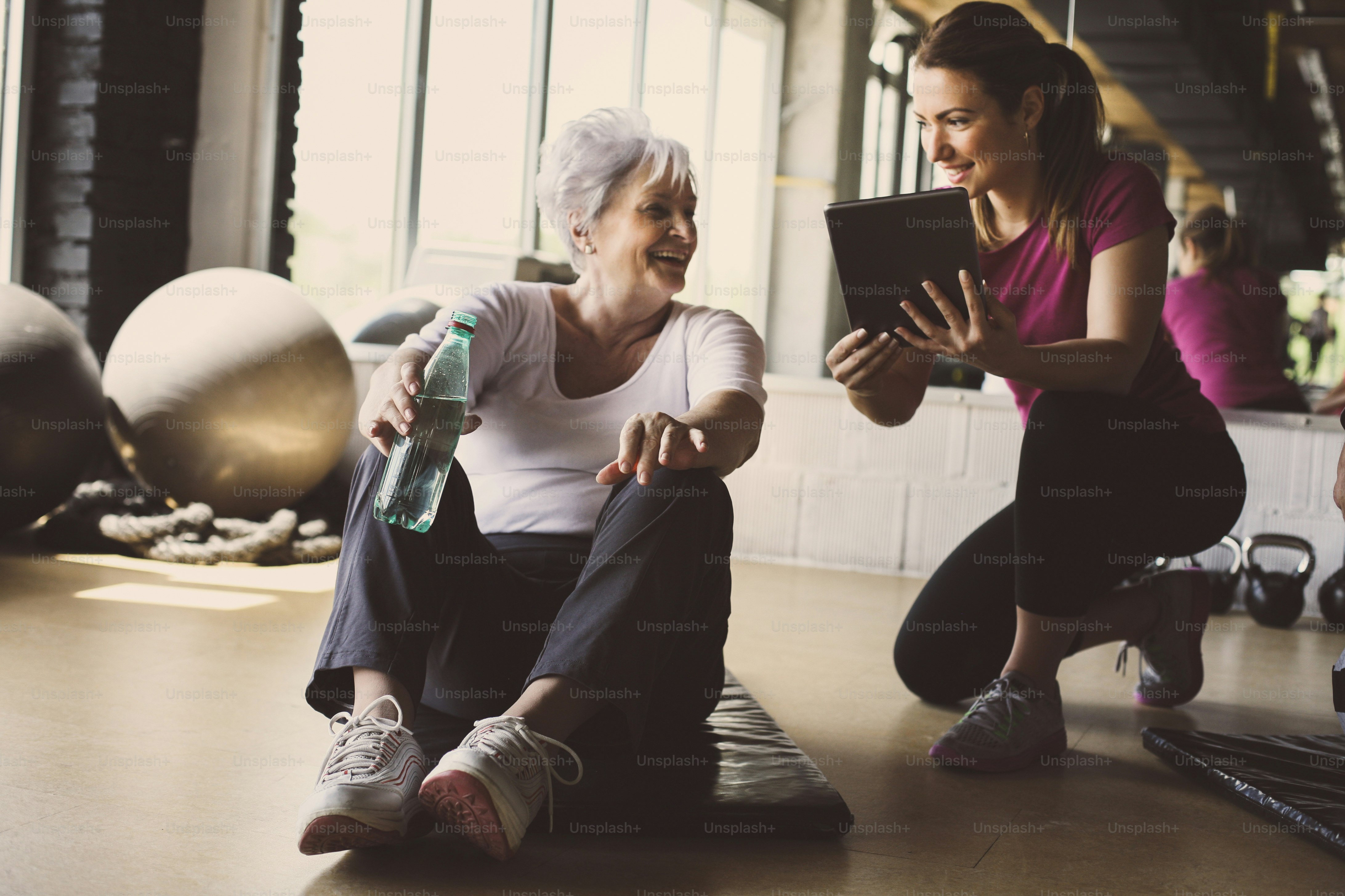 Senior woman workout in rehabilitation center. Personal trainer showing something  on digital tablet.