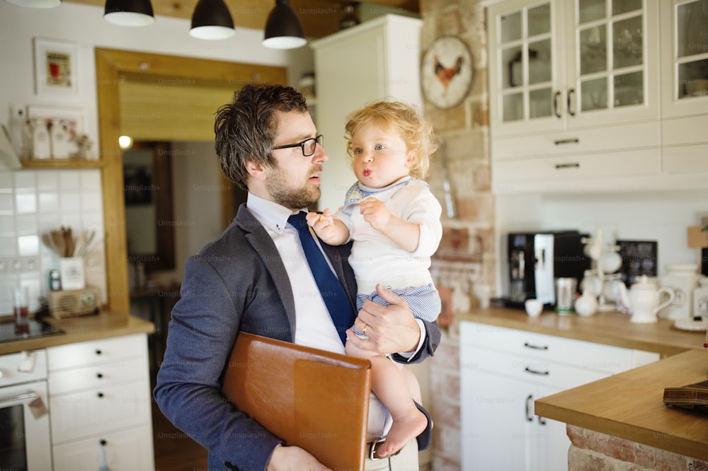 Young businessman coming home from the office, holding his little son in the arms.