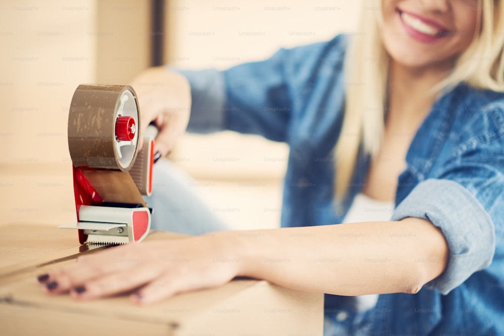 Caucasian girl taping boxes for moving in new apartment