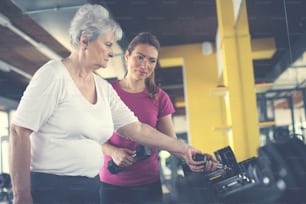 Personal Trainer Arbeitsübung mit älteren Frauen im Fitnessstudio. Frau nimmt Gewicht. Workout im Fitnessstudio