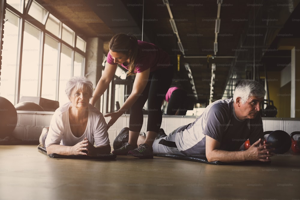 Treino de casal sénior em centro de reabilitação. Personal trainer ajuda casal de idosos a fazer alongamento no chão.
