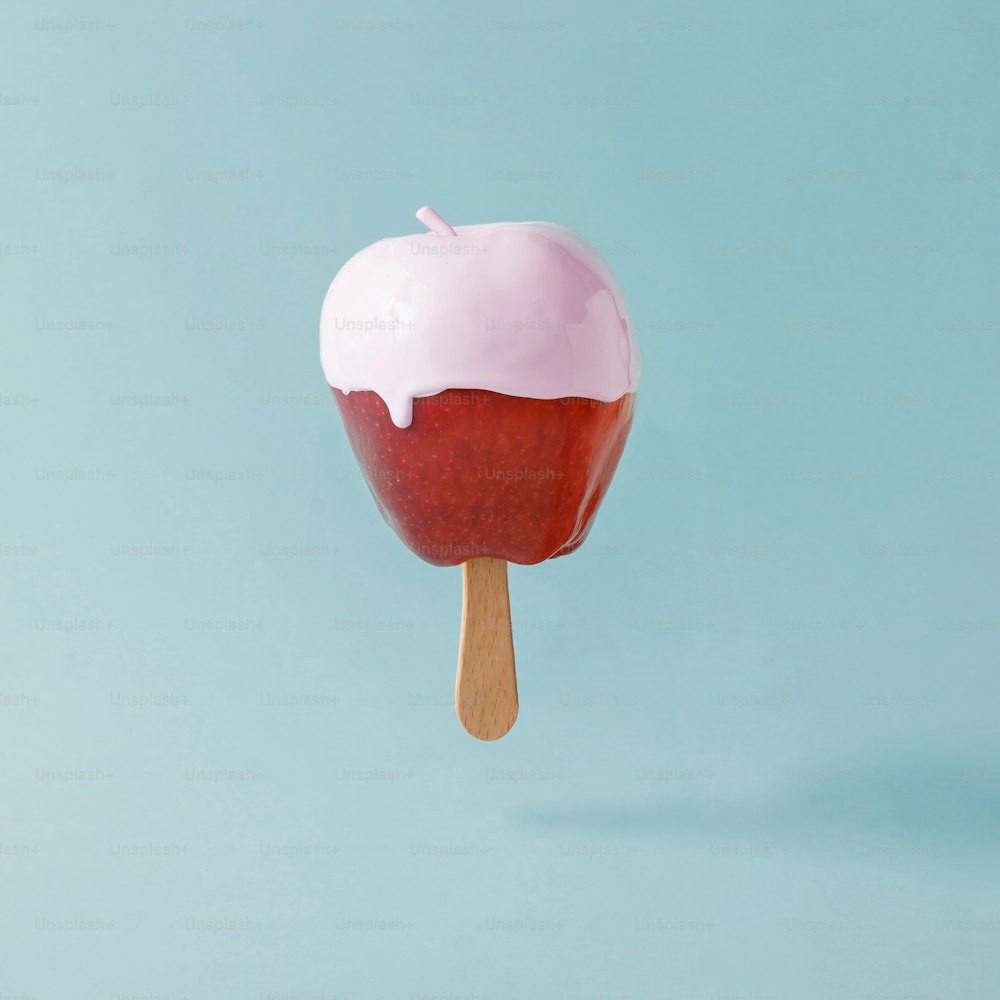 Roter Apfel mit Eisstange auf pastellblauem Hintergrund. Kreatives Food-Konzept.