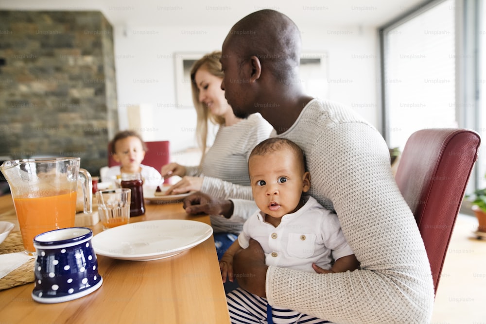 Belle jeune famille interraciale à la maison avec leur jolie fille et leur petit garçon prenant le petit déjeuner ensemble.