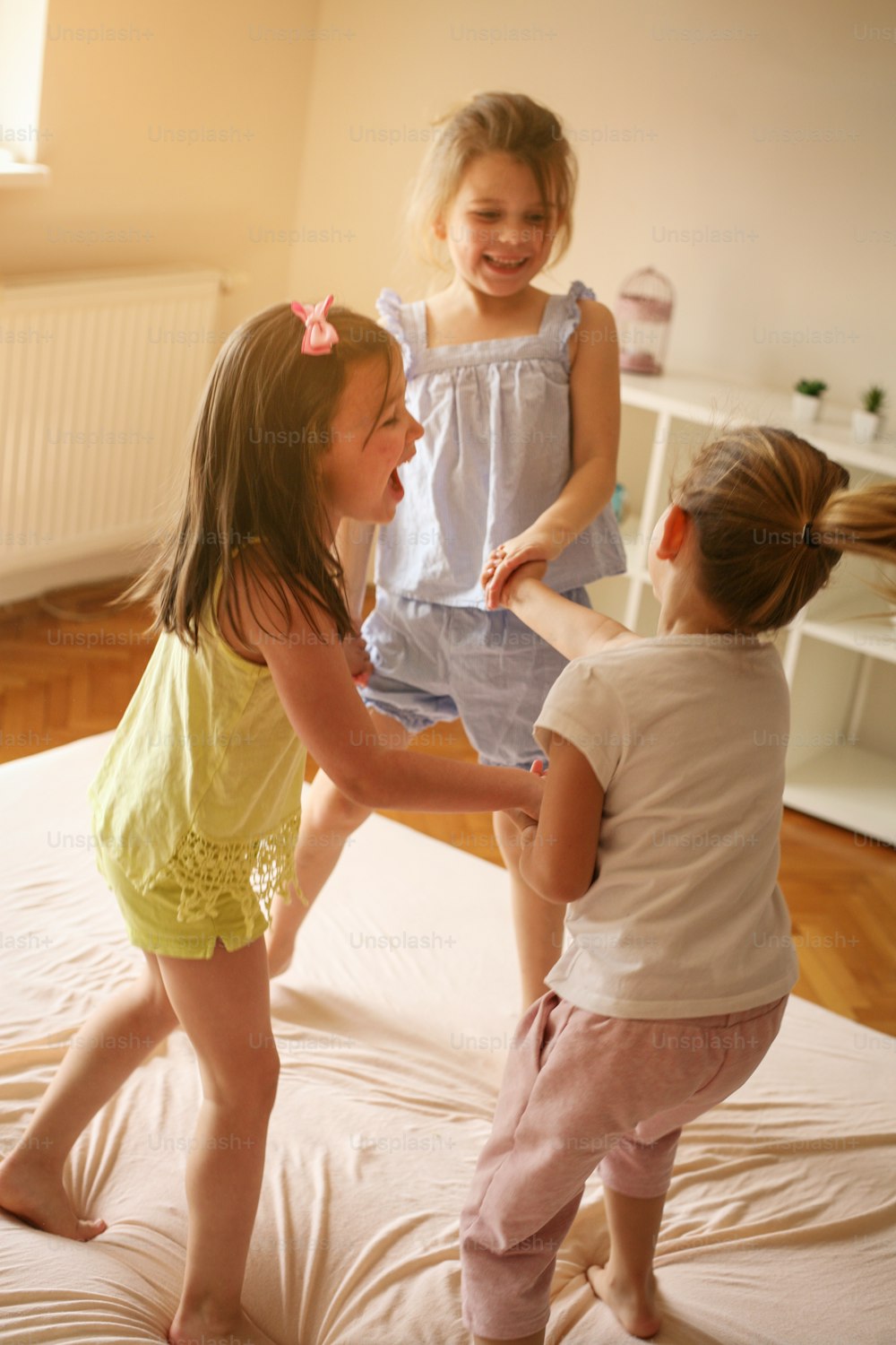 어린 소녀들이 침대에서 함께 즐거운 시간을 보내고 있습니다. 어린 소녀들은 침대에서 집에서 놀고 있습니다.