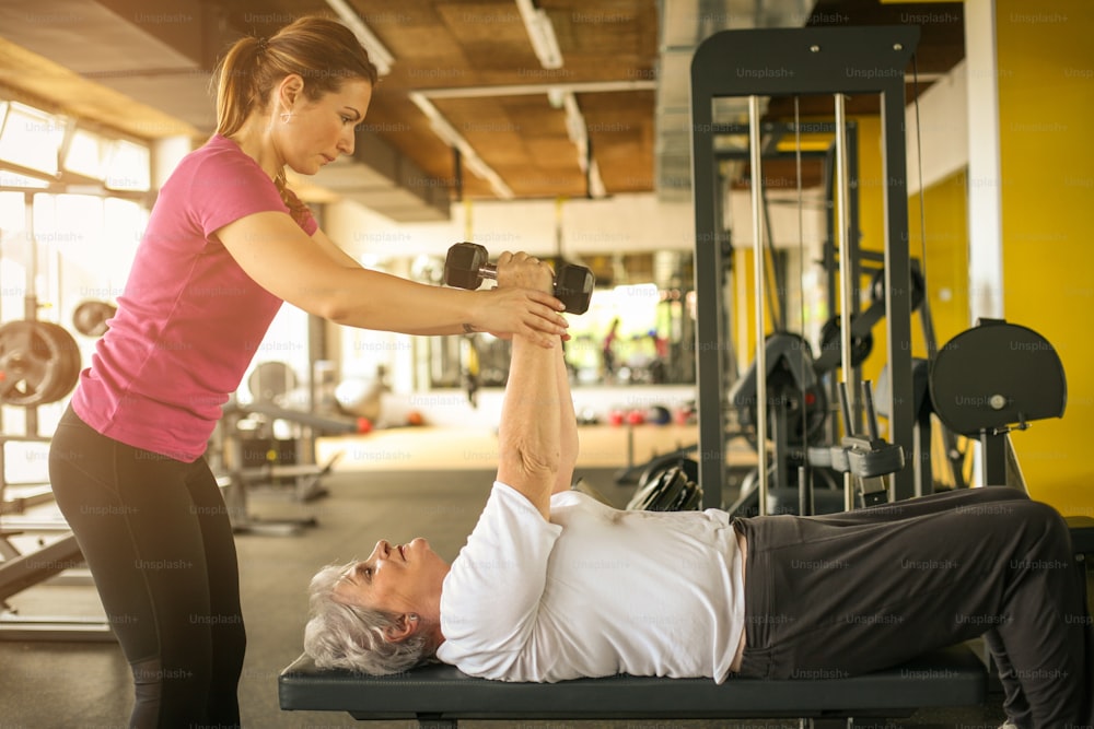 Personal trainer working exercise with senior woman in the gym. Woman lift weight. Workout in gym.