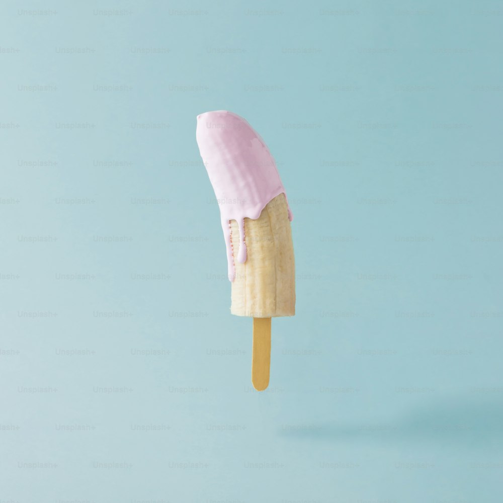 Banane mit Eisstange auf pastellblauem Hintergrund. Kreatives Food-Konzept.