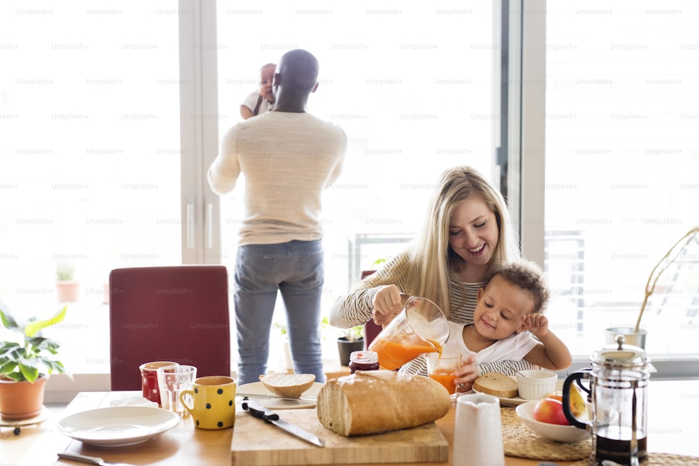 Linda família inter-racial jovem em casa com sua filha fofa e filho pequeno tomando café da manhã juntos.