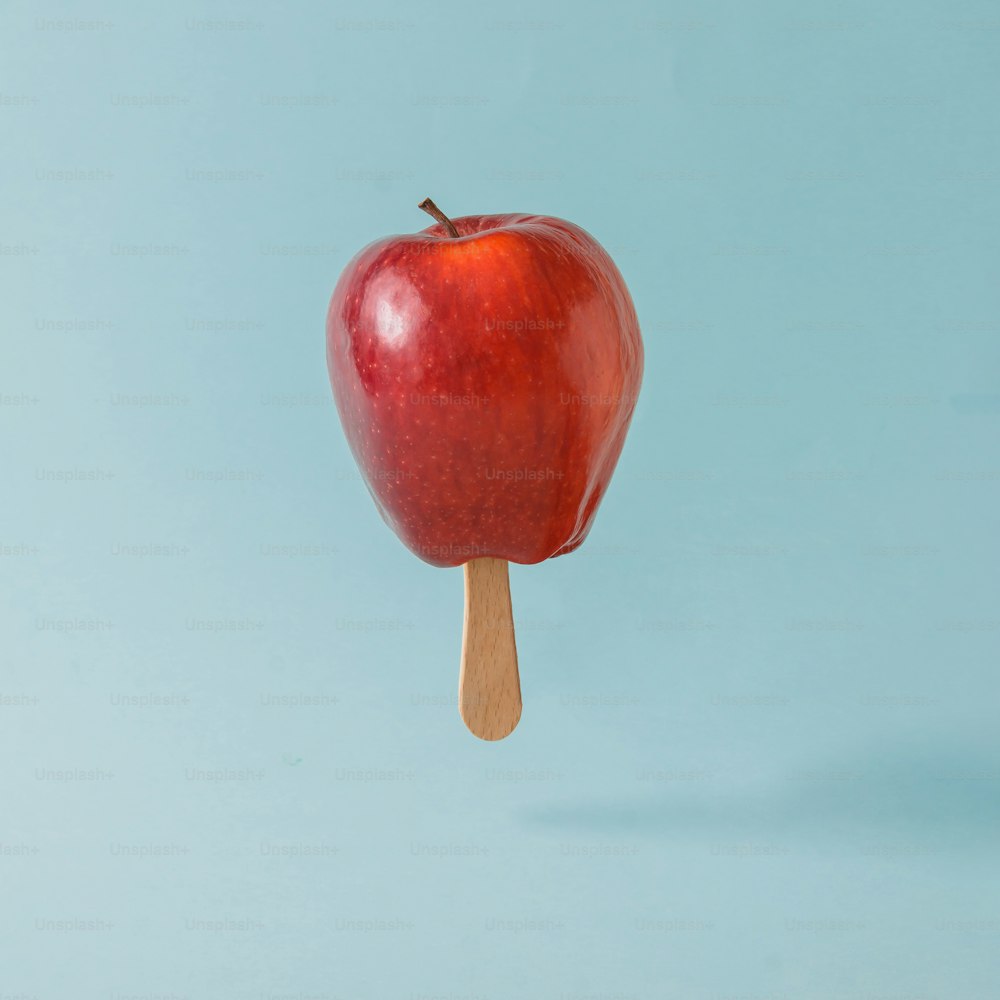 파스텔 블루 배경에 아이스크림 스틱이 있는 빨간 사과. 음식 창조적 인 개념입니다.