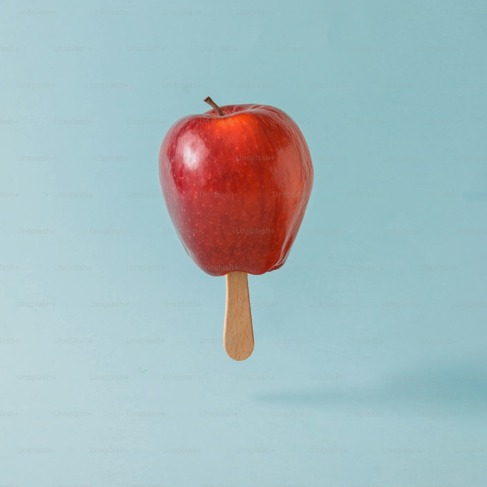 Maçã vermelha com palito de sorvete no fundo azul pastel. Conceito criativo de alimentos.