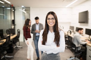 Geschäftsfrau posiert im Büro, während andere Geschäftsleute im Hintergrund sprechen