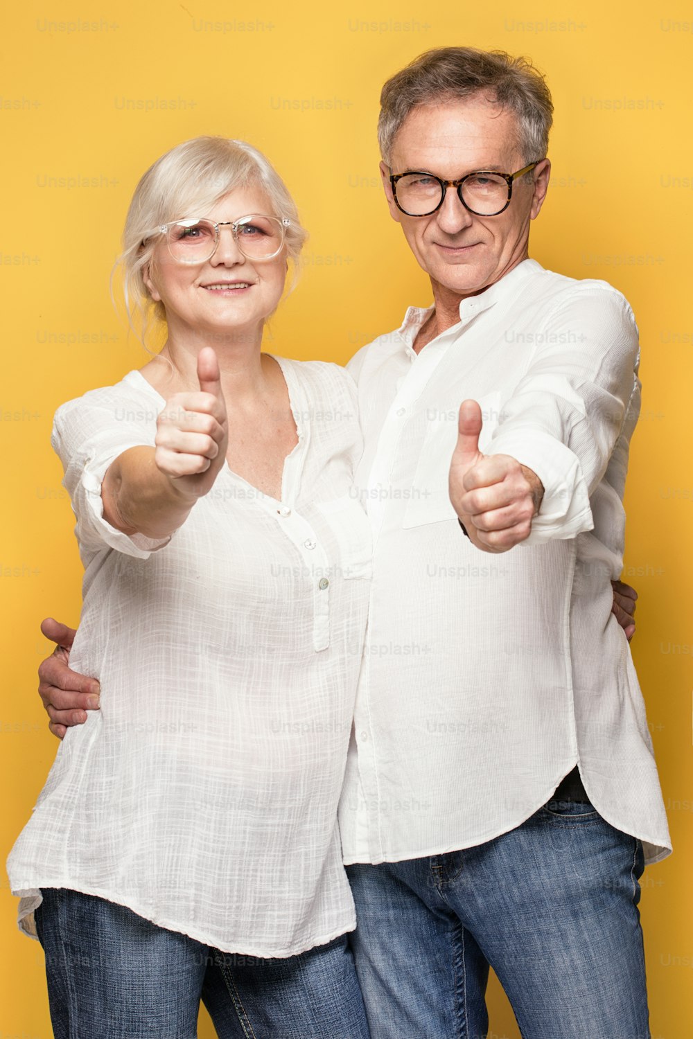 Beautiful happy senior couple posing together on yellow background, showing ok sign.