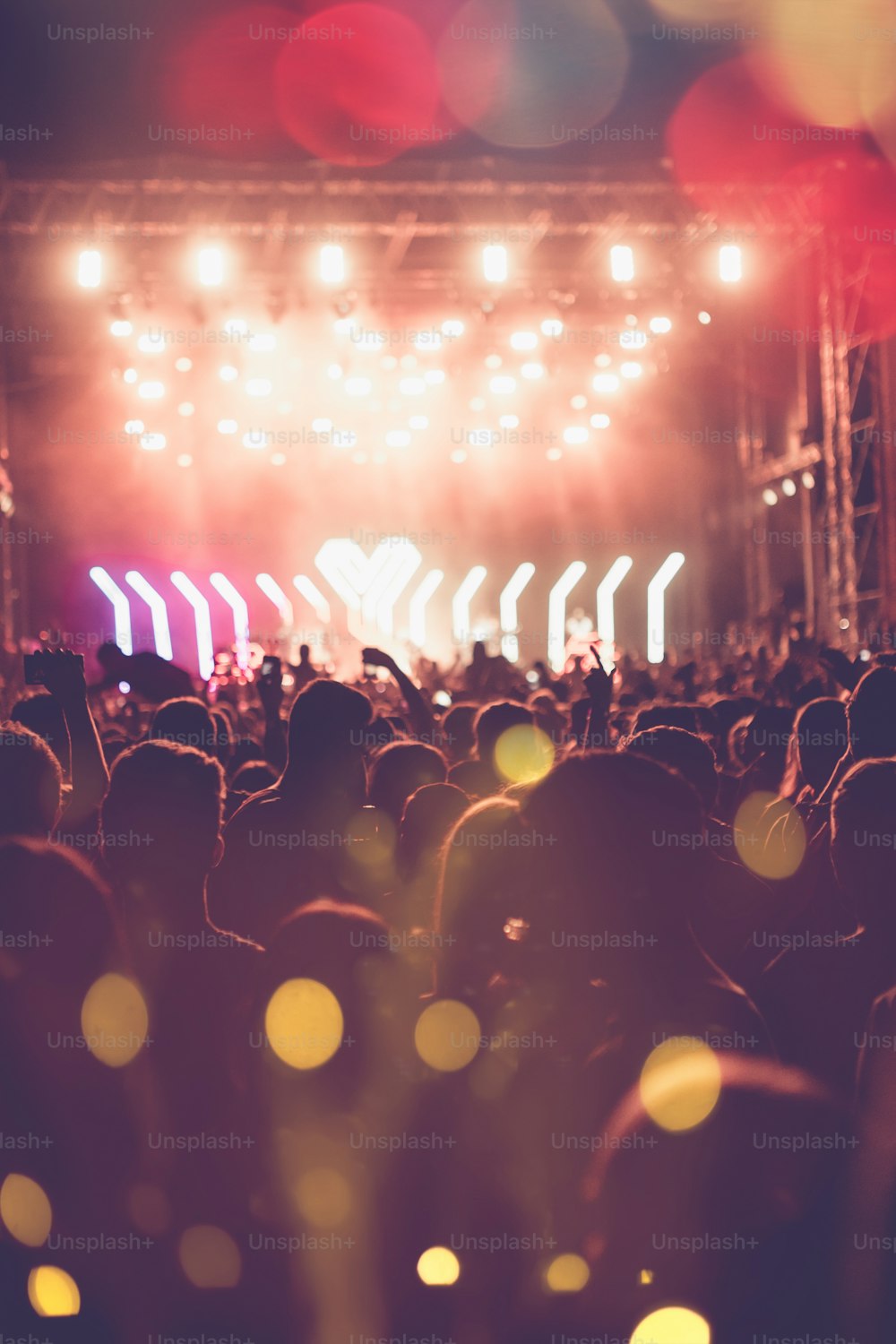 Silhouettes of festival concert crowd in front of bright stage lights. Unrecognizable people and colorful effects.