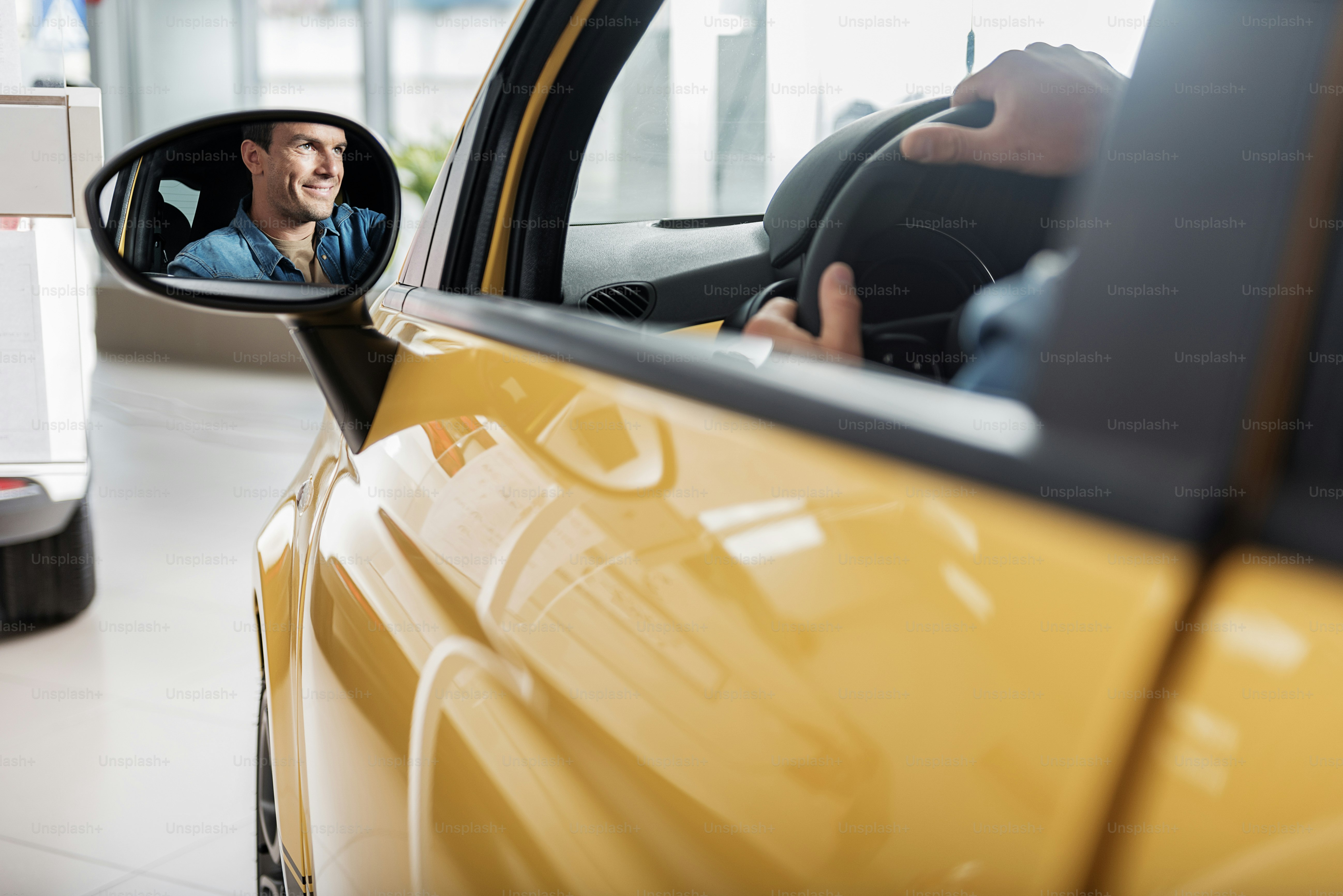 陽気な男性を映し出すサイドミラーをクローズアップします。彼は新しい自動車を運転しています