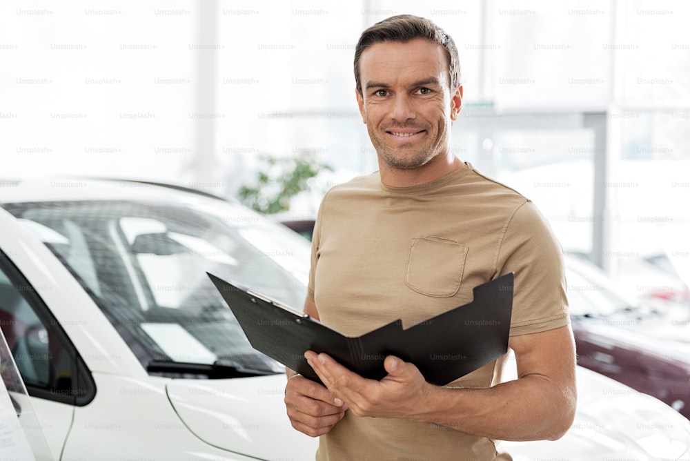 Portrait of man expressing cheerfulness while looking through contract in car dealership. He looking at camera