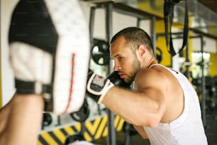 권투 선수는 스파링 파트너의 글러브를 치고 있습니다. 남자들은 체육관에서 운동한다.
