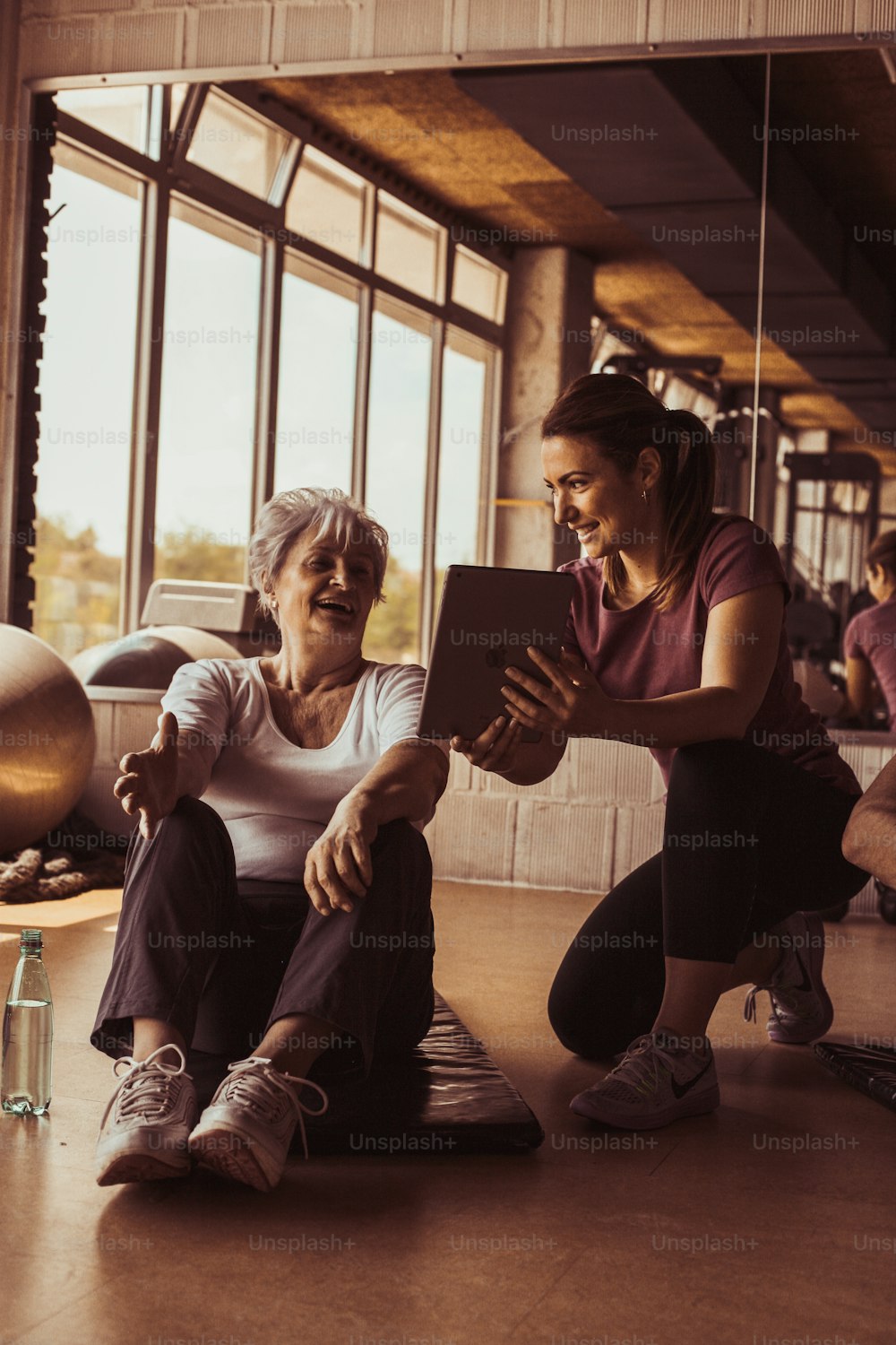 Senior woman workout in rehabilitation center. Personal trainer showing something  on digital tablet.