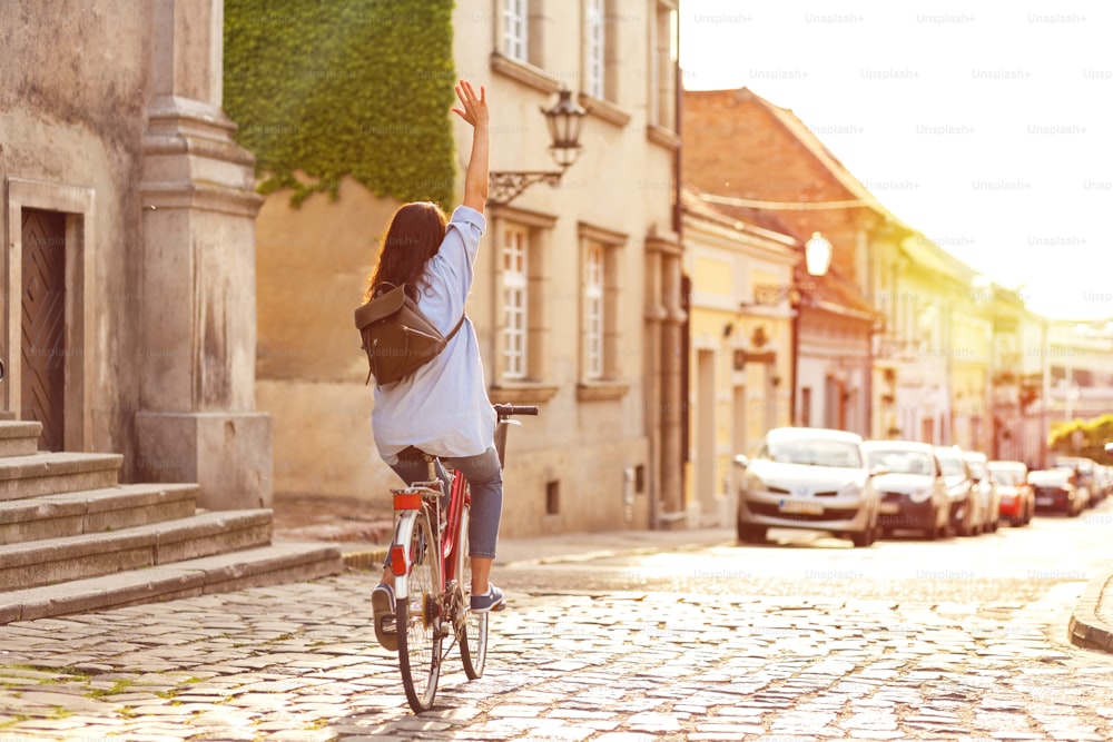 Rear view of young woman riding a bicycle down the street at sunset.