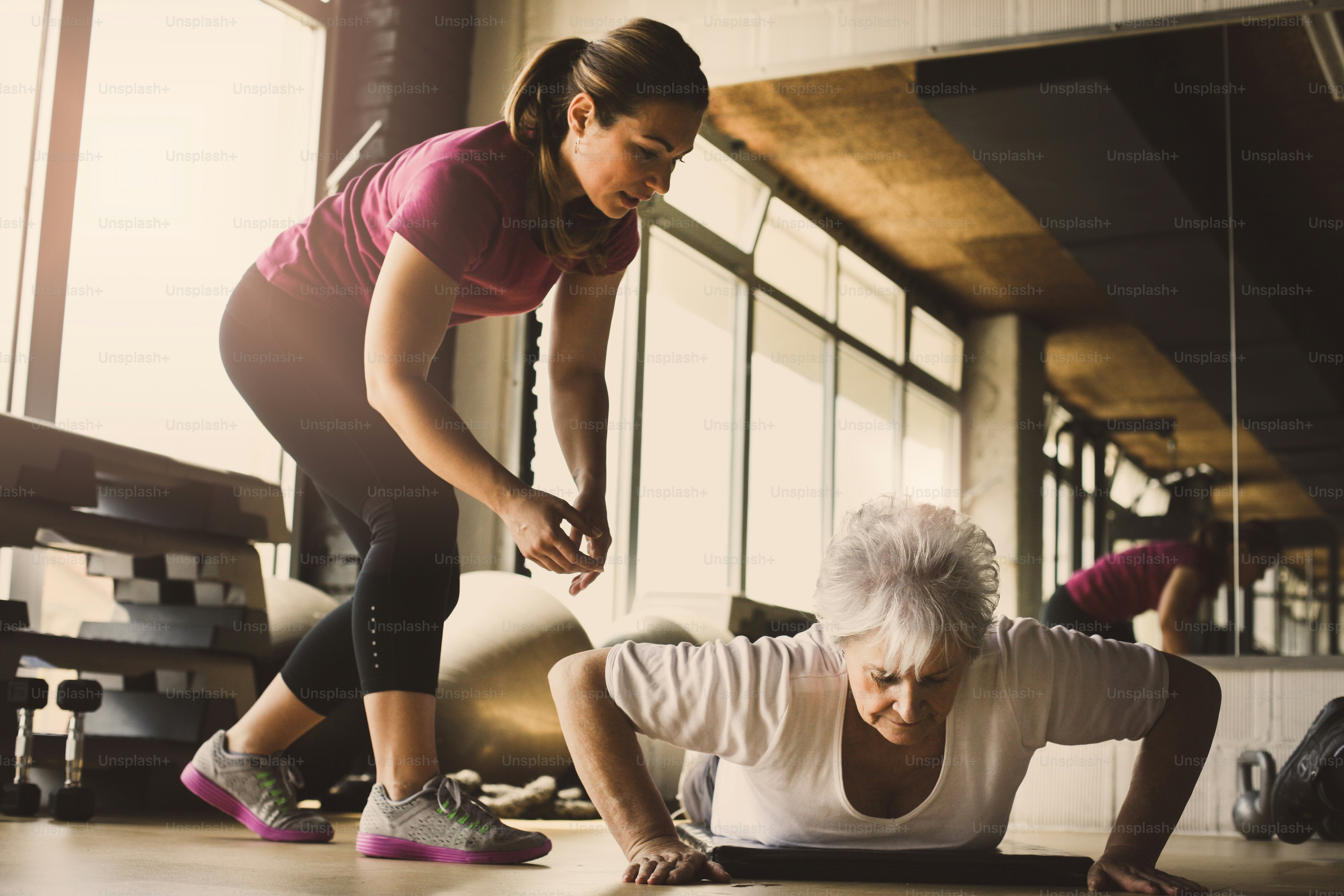 Older women doing pushups. Young personal trainer helping senior woman. Workout in rehabilitation center.