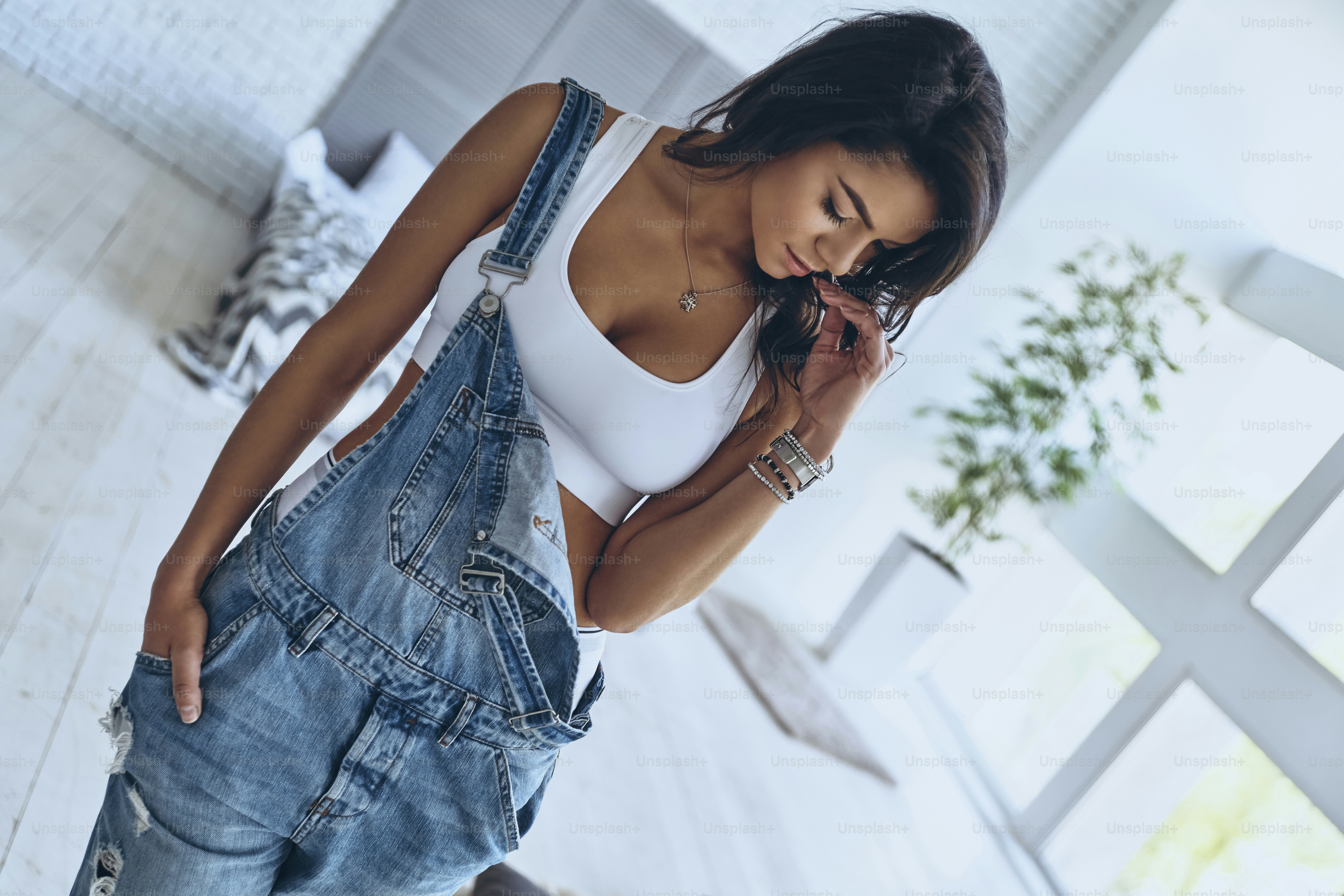 Full length of beautiful young woman keeping hand in pocket and touching her hair while standing in the bedroom at home