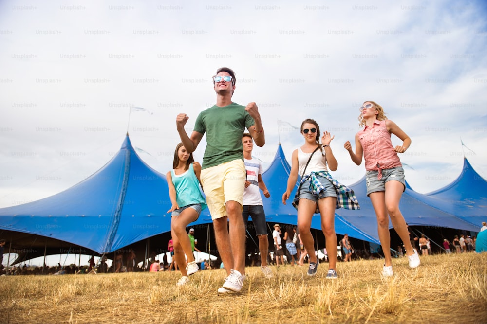 Group of teenage boys and girls at summer music festival, dancing in front of big tent, sunny day