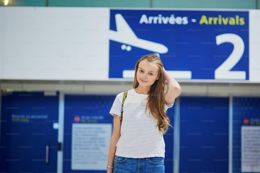Schönes junges Touristenmädchen mit Rucksack und Gepäck am internationalen Flughafen, an der Ankunftstür