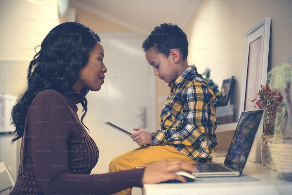 기술을 사용하는 어머니와 아들. 집에서 노트북을 사용하는 아프리카계 미국인 여성과 그녀의 아들