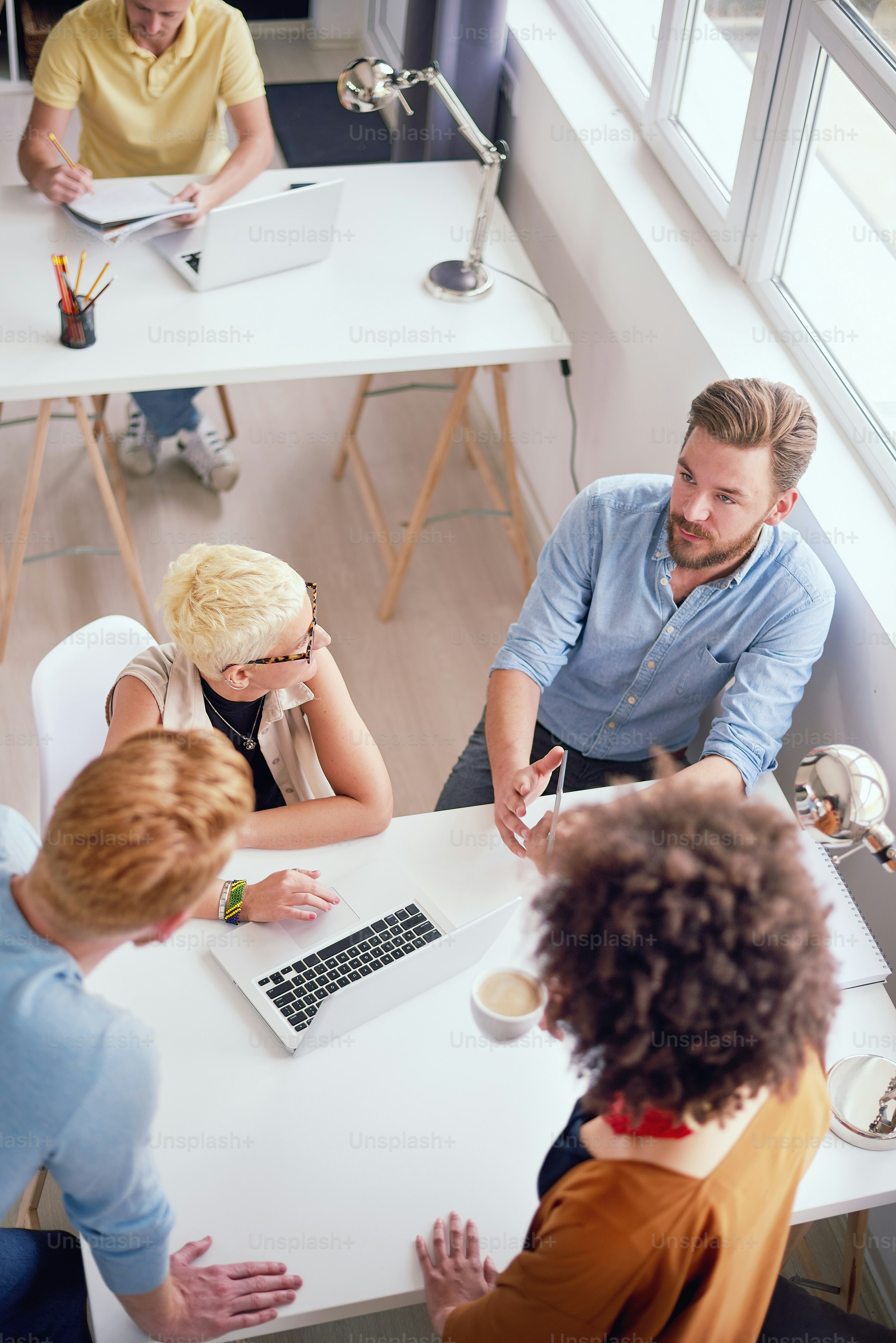 Multi - ethnic team sitting and standing around desk while having presentation in modern office