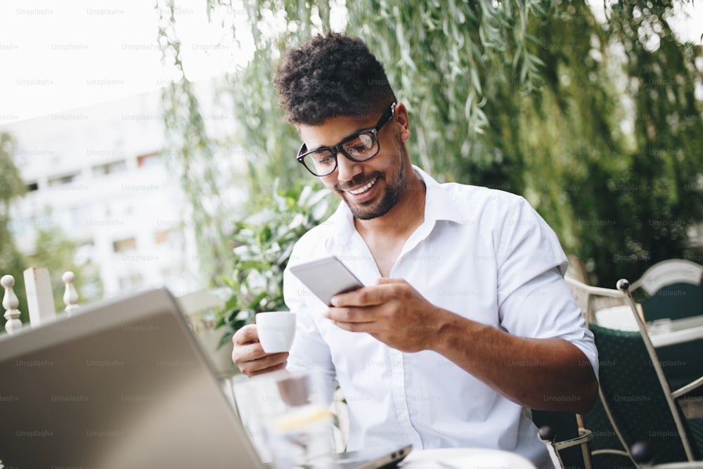 Young attractive Afro American businessman sitting in cafe bar doing some work on laptop and taking on mobile phone.