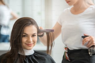 Young female sitting in hair salon hairdo styling brush