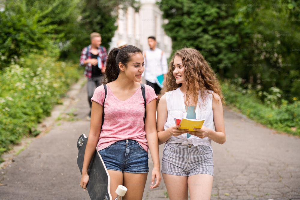Grupo de quatro estudantes adolescentes atraentes que caminham da universidade.