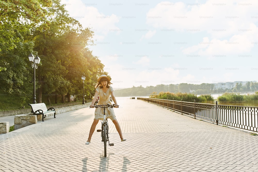 Portrait de mode en plein air d’une jolie jeune brune dans un chapeau sur un vélo.