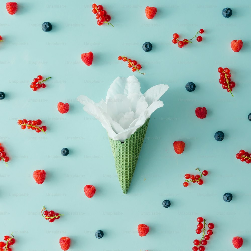 White flower in ice cream cone with forest fruit pattern. Flat lay. Summer concept.