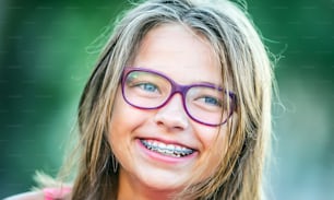 Chica sonriente feliz con aparatos dentales y gafas. Joven linda chica rubia caucásica con aparatos dentales y gafas.