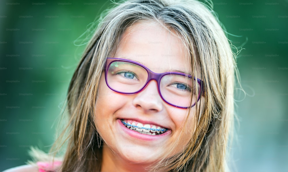 Happy smiling girl with dental braces and glasses. Young cute caucasian blond girl wearing teeth braces and glasses.