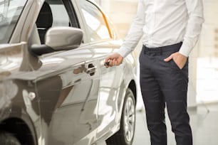 Young man standing near the car opening door rental service