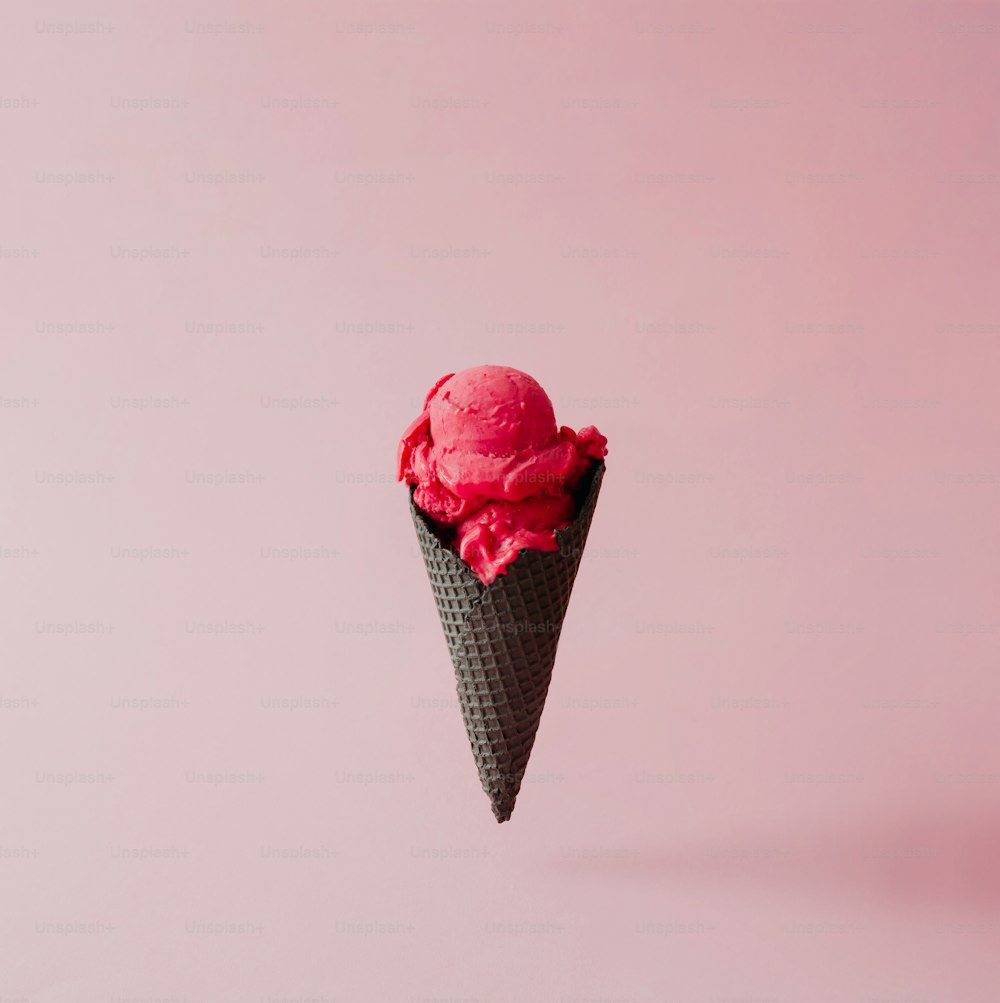 ピンクのパステルカラーの背景に黒い円錐形のイチゴアイスクリーム。夏のクリエイティブなコンセプト。