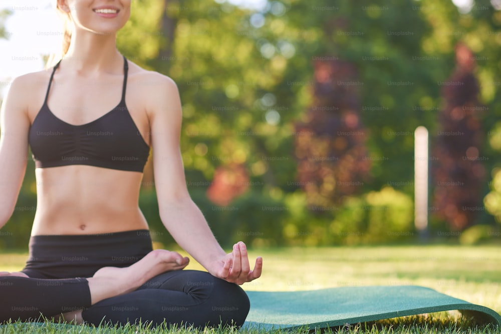 Zugeschnittene horizontale Aufnahme einer jungen Frau, die freudig lächelt und Yoga im Park kopiert Glücksharmonie Balance Asana-Konzept.
