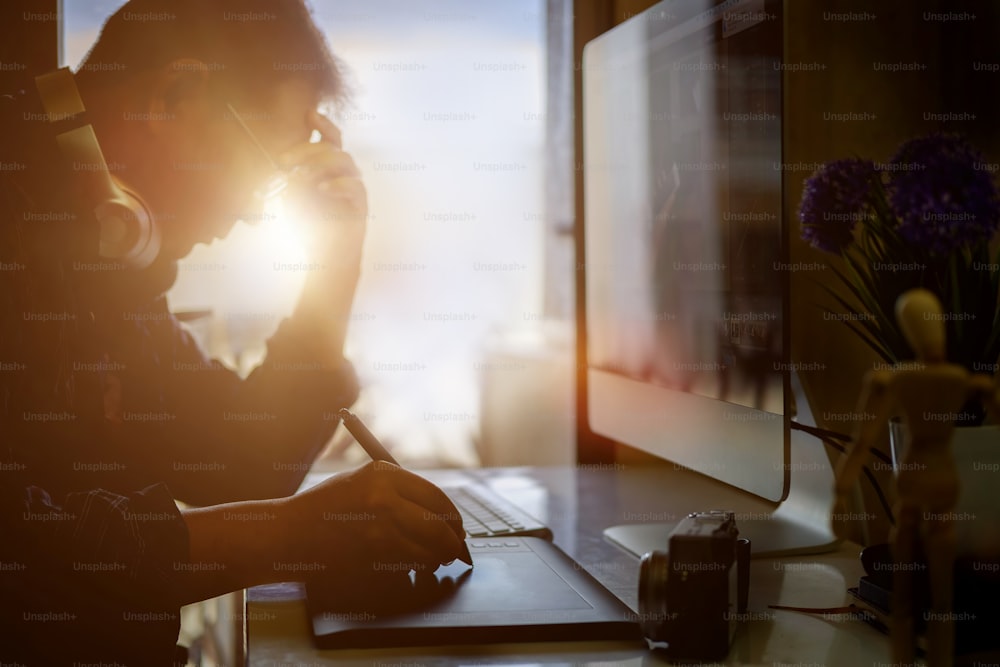 현대 사무실에서 일하는 동안 디지털 그래픽 태블릿을 사용하는 스트레스를 받는 힙스터 그래픽 디자이너 남자, 나무 테이블이 있는 현대적인 작업 공간에 앉아 있는 전문 남성 리터쳐의 사진.
