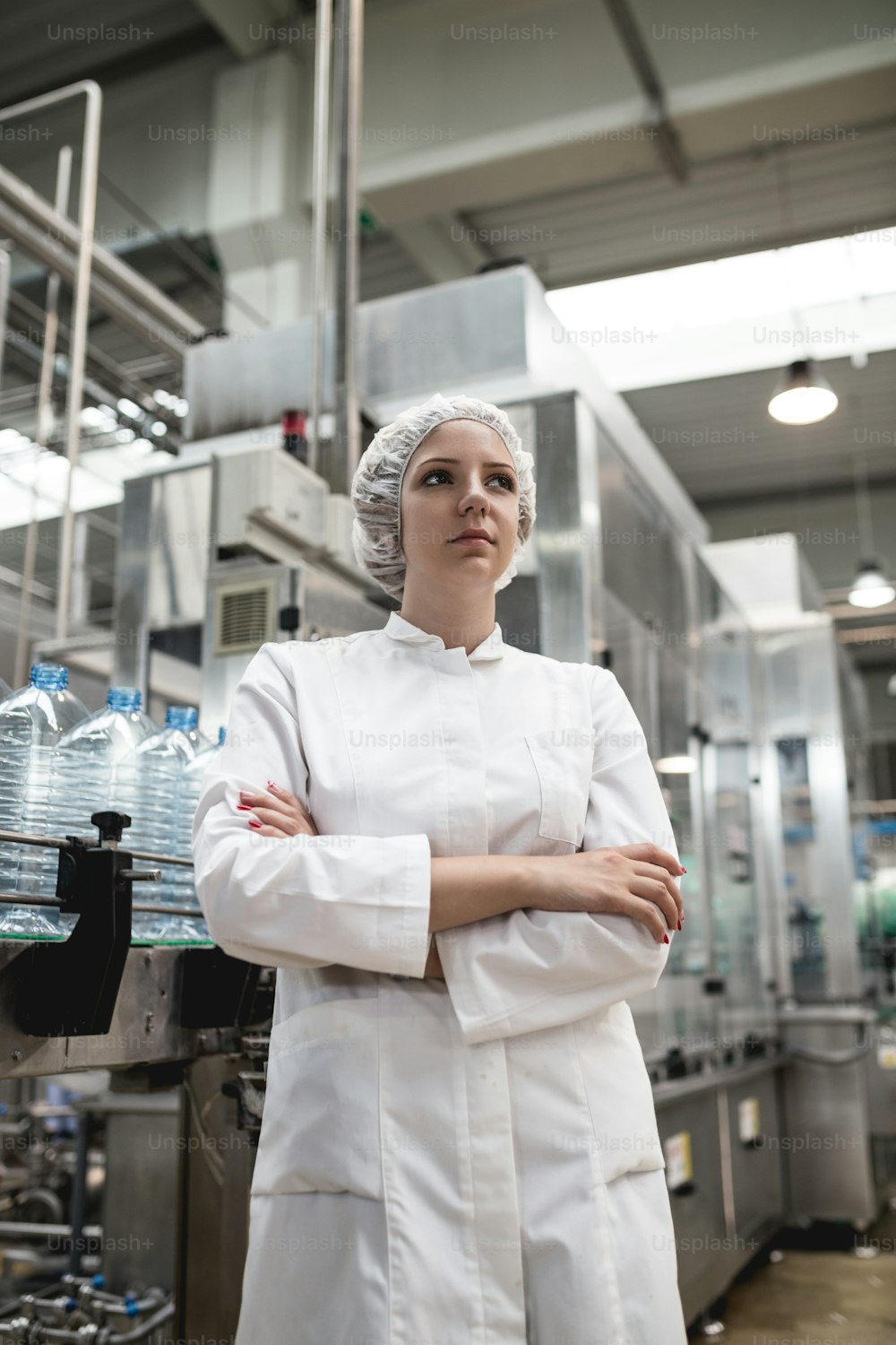 Young happy woman worker checking robotic line for bottling and packaging pure drinking water into bottles and canisters.