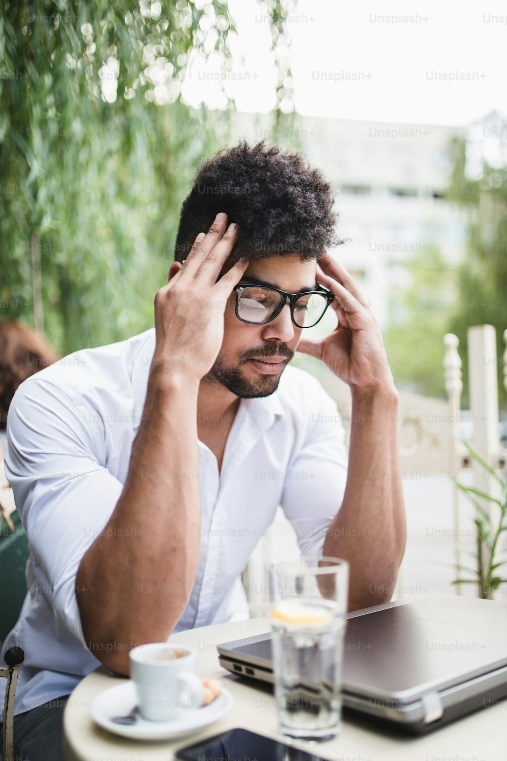 Hombre de negocios afroamericano serio y preocupado con anteojos sentado en un café y pensando con los ojos cerrados.