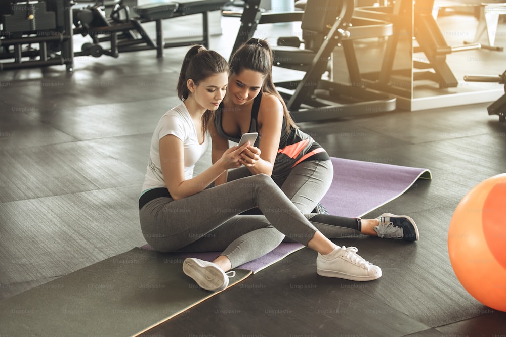 Junge Freundinnen trainieren im Fitnessstudio und surfen mit dem Smartphone
