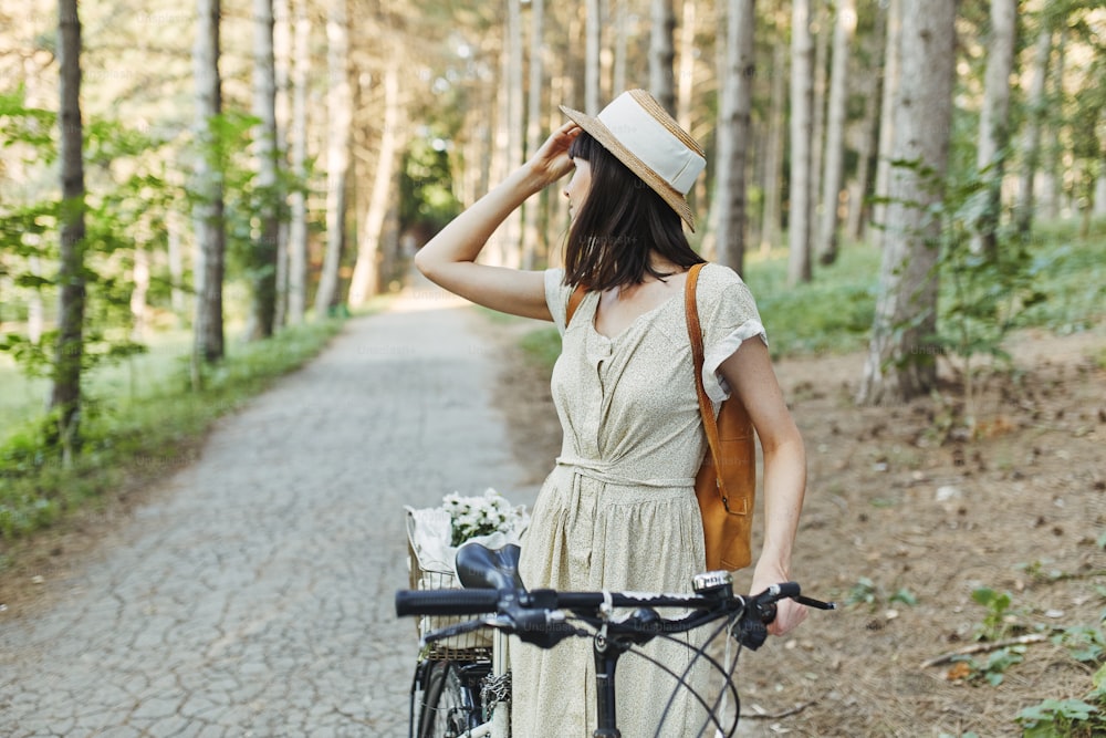 Ritratto di moda all'aperto di attraente giovane bruna in un cappello su una bicicletta.