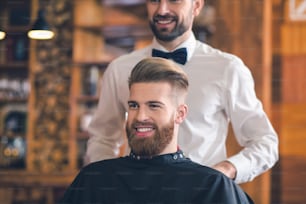 Junger Mann sitzt im Friseursalon und bereitet sich fröhlich auf den Haarschnitt vor