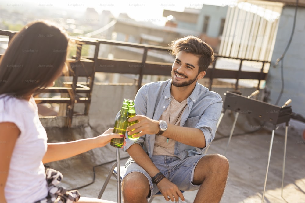 Young couple enjoying hot summer day at a rooftop party, drinking beer and having fun