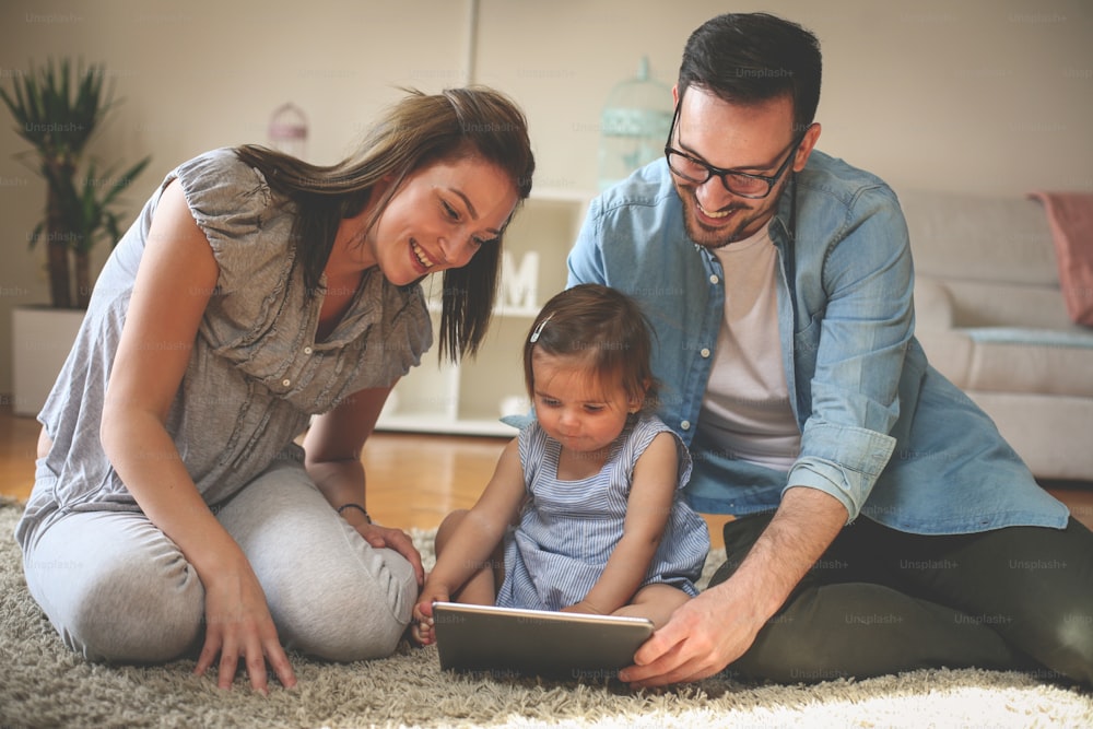 赤ん坊を連れて床に横たわる家族。床で一緒にデジタルタブレットを使う家族。